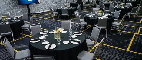 Un salón de conferencias con varias mesas dispuestas para comer, equipado con sillas y una pantalla grande que muestra 'TL'.