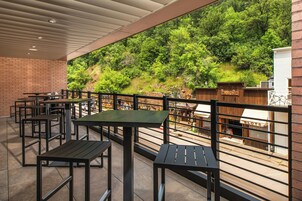 Un patio exterior con mesas y sillas, una valla de madera y vistas a una ladera boscosa.