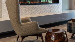 A modern living room with a flat-screen TV mounted on a textured wall, a fireplace, a comfortable armchair, and a wooden coffee table.