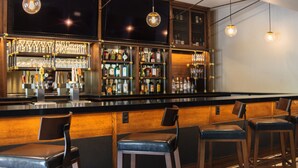 A bar area with wooden bar counters, multiple stools, and shelves stocked with bottles.