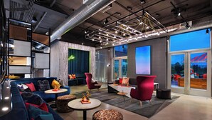 Ein moderner Lounge-Bereich mit Sofas, Sesseln und runden Tischen, mit einem großen Fenster und Blick auf die Stadt.