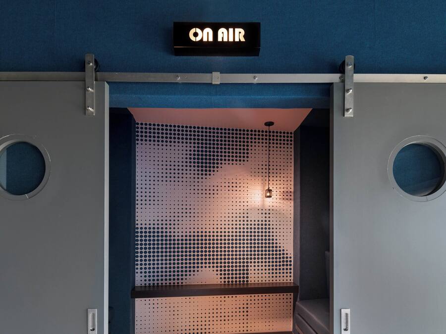 A room with a perforated metal partition, a sign reading "ON AIR", and circular windows on either side.