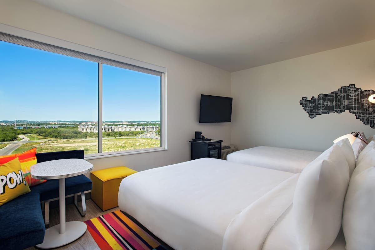 Une chambre d’hôtel dotée d’une grande fenêtre, d’un téléviseur à écran plat, d’un canapé, d’une petite table et d’un lit avec une literie blanche.