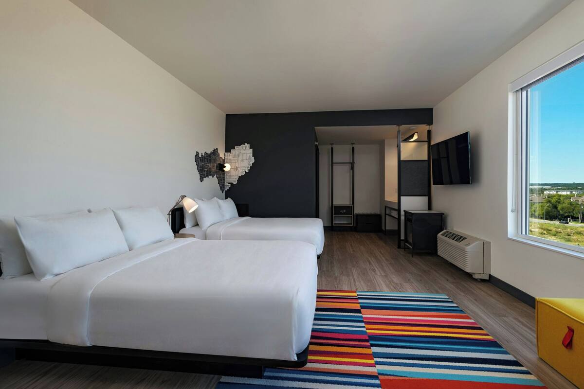 Une chambre d’hôtel moderne avec deux lits, une grande fenêtre, un téléviseur à écran plat et une vue sur la ville.