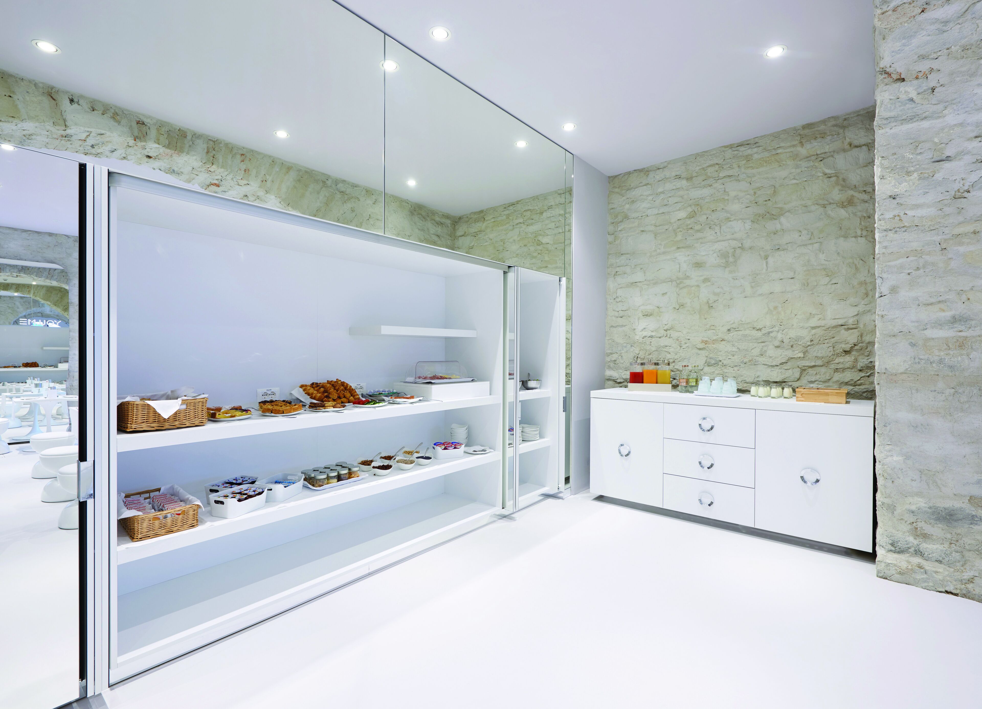 A modern, well-lit room with a glass partition, white cabinets, and a stone wall.