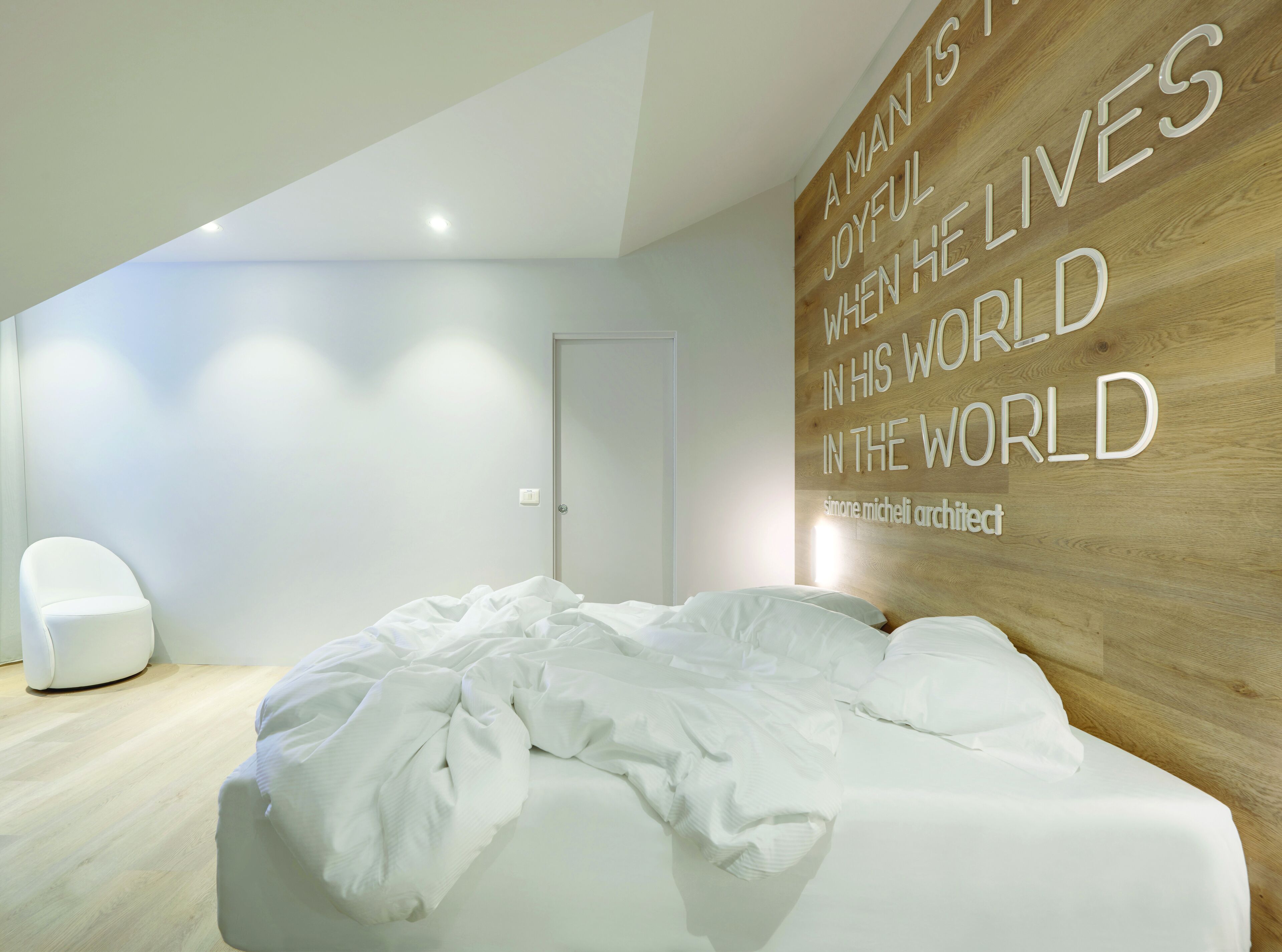 A modern bedroom with a wooden accent wall, a white bed, and a minimalist chair.