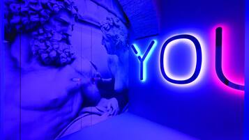 A neon sign with the letters "YO" in blue and pink, set against a wall with a classical sculpture.