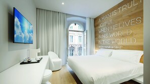 A modern hotel room with a large bed, a desk, and a view of a building through an arched window. - You.Me Design Place Hotel (Trieste)