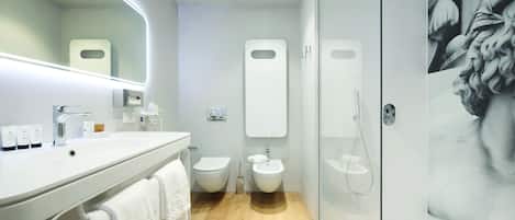 Un baño moderno con un espejo grande, un lavamanos, dos inodoros, un bidé y una ducha con mampara de vidrio.