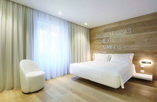 Camera da letto moderna con un letto grande, una sedia bianca e una parete in legno con una citazione motivazionale.