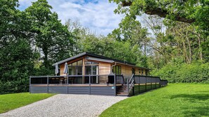 A modern cabin with a covered deck, a gravel pathway, and lush greenery surrounding it. - Cedar Lodge | sleeps 8 - Hot Tub, Dog Friendly - 5* Gold Award (PICKERING)