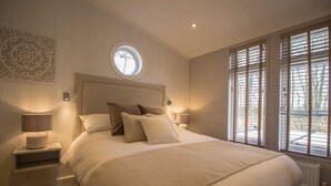 A bedroom with a large bed, two bedside lamps, a round window, and a radiator. - Cedar Lodge | sleeps 8 - Hot Tub, Dog Friendly - 5* Gold Award (PICKERING)