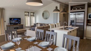 A modern kitchen with a central island, stainless steel appliances, and a dining area set for six with a wooden table and chairs. - Cedar Lodge | sleeps 8 - Hot Tub, Dog Friendly - 5* Gold Award (PICKERING)