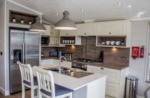Une cuisine moderne dotée d’un îlot central, d’appareils électroménagers en acier inoxydable et de luminaires suspendus.