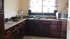 A kitchen with dark wooden cabinets, a granite countertop, a coffee maker, a microwave, and a window with a curtain. - Vistas del Tenorio (Tierras Morenas)