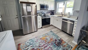 A kitchen with white cabinets, stainless steel appliances, a colorful rug, and a decorative ceiling. - Ivy's Cottage- Renovated, In Town. Great Location. (Chincoteague)