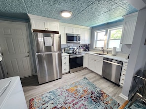 A kitchen with white cabinets, stainless steel appliances, a colorful rug, and a decorative ceiling.