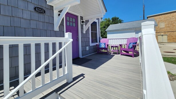 A wooden deck with a white railing, a purple door, and two Adirondack chairs with cushions. - Ivy's Cottage- Renovated, In Town. Great Location. (Chincoteague)