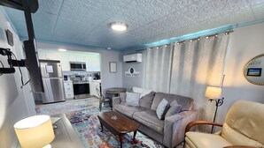 A compact living space with a kitchenette, a sofa, a coffee table, and a dining table. - Ivy's Cottage- Renovated, In Town. Great Location. (Chincoteague)