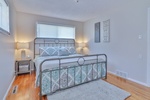 A bedroom with a metal bed frame, a bedside table with a lamp, a window with blinds, and motivational wall art. - Newly Remodeled SLC Home close to Downtown (Salt Lake City)