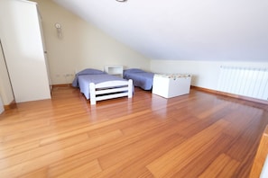 A bedroom with a wooden floor, a bed, a small white chest of drawers, and a radiator.