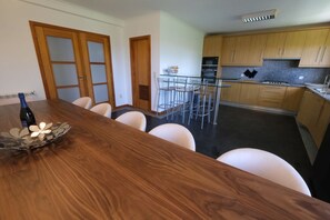 A modern kitchen with wooden cabinets, a stainless steel refrigerator, and a dining area with a wooden table and white chairs.