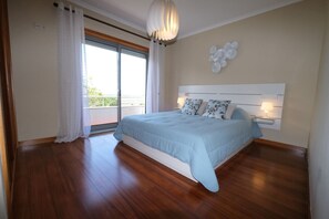 A bedroom with a large bed, a ceiling light fixture, a view of the outdoors, and a wall-mounted lamp.