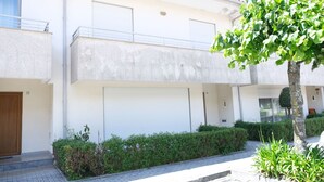 Un immeuble résidentiel à deux étages, doté d’un garage fermé, d’un balcon et d’une haie bien entretenue.