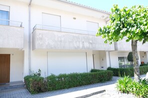 A two-story residential building with a closed garage door, a balcony, and a well-maintained hedge.