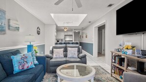 Una sala de estar con sofá, sillón, mesa de centro, estantería y televisor.