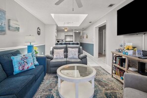 A living room with a sofa, armchair, coffee table, bookshelf, and a TV.