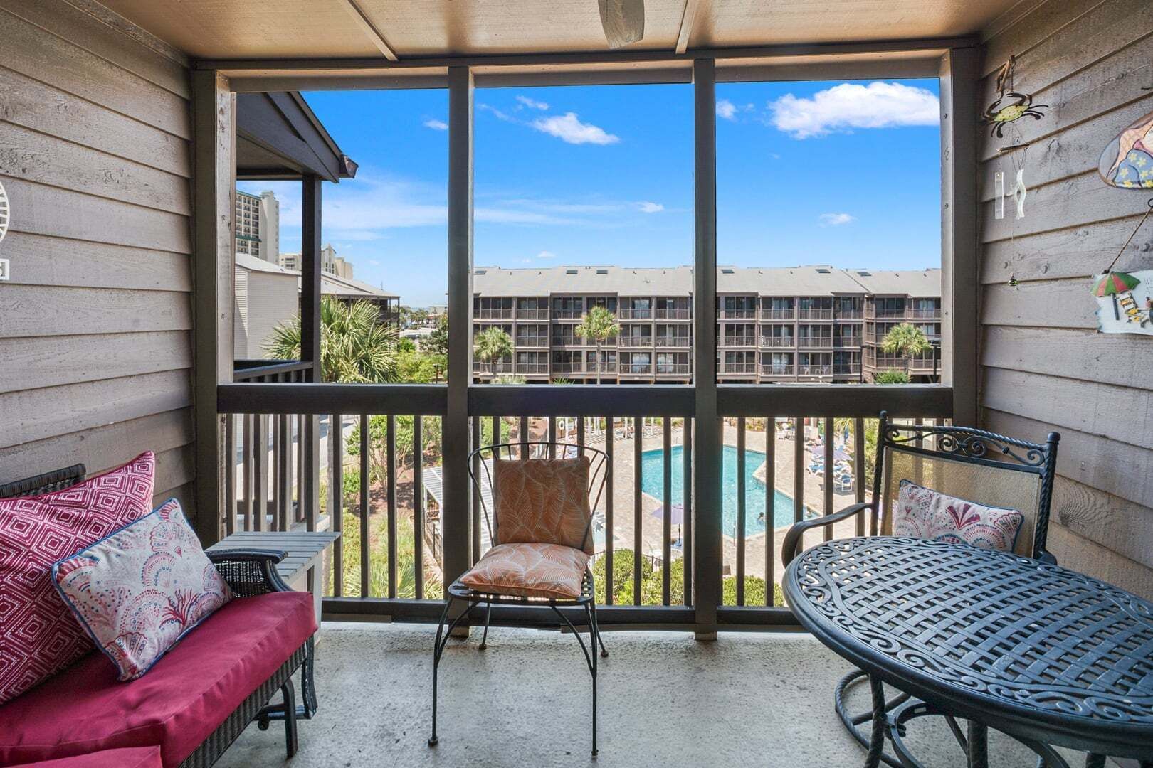 Ein Balkon mit Blick auf einen Swimmingpool und Gebäude, ausgestattet mit einer Couch, Stühlen und einem Tisch.