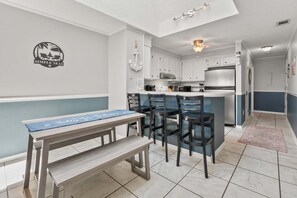 A compact kitchen with a dining area, featuring a bench, chairs, and a small island with bar stools.