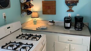 A compact kitchen with a gas stove, a coffee maker, and a wall-mounted mug rack.