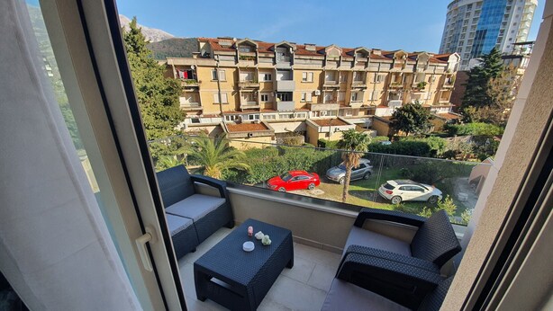 Un balcon aménagé avec du mobilier d’extérieur, une vue sur un quartier résidentiel avec des immeubles à plusieurs étages et des voitures garées.