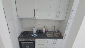 Une cuisine de taille réduite avec des meubles blancs, une cuisinière, un four et un évier.