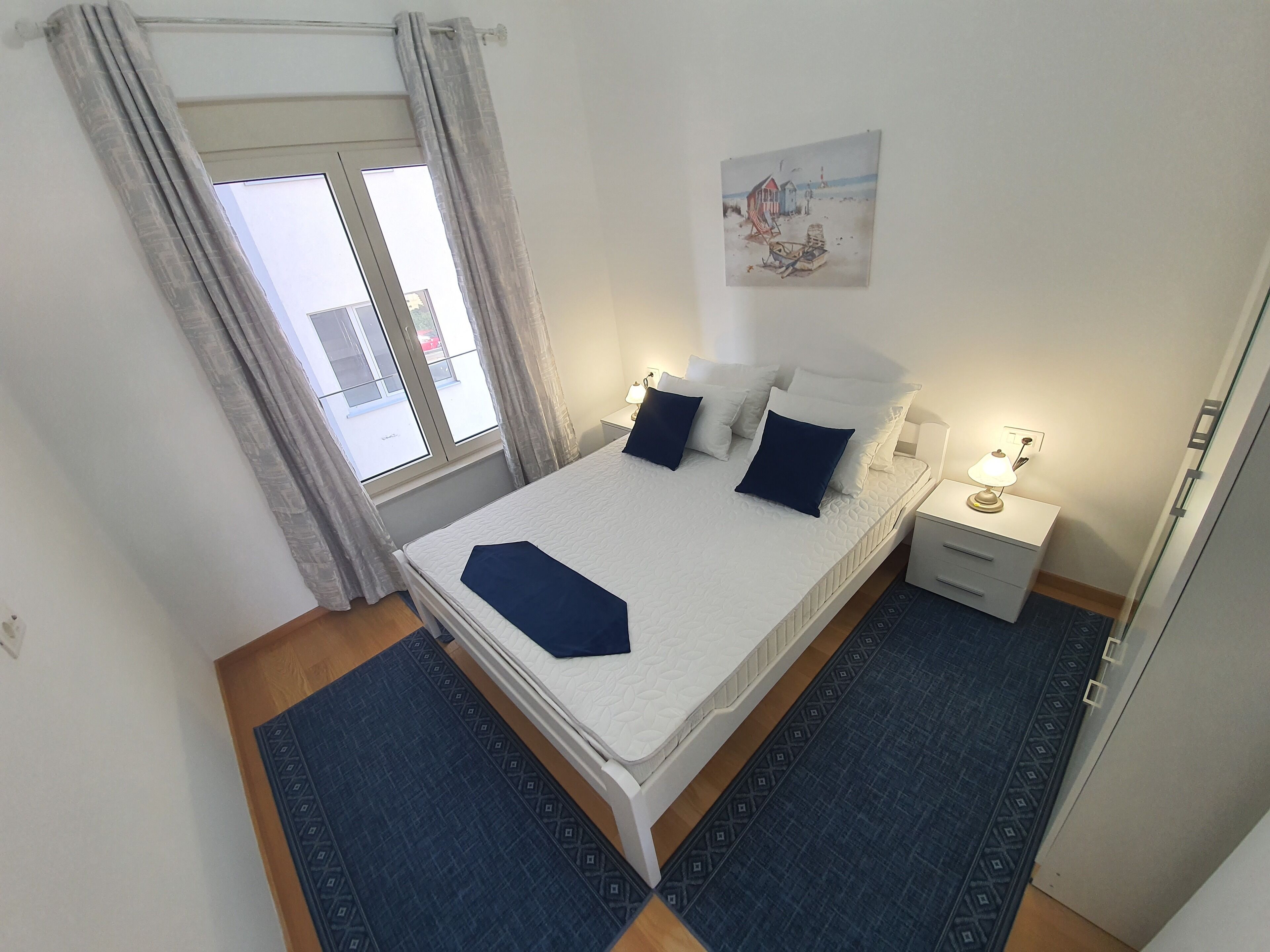 A bedroom with a bed, bedside tables, a lamp, a painting on the wall, and a window with curtains.