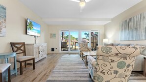A spacious living room with a large TV, comfortable seating, and a view to the outside. - Book 3 Nights & Get 1 Night Free* Charming Cottage*6 Seat Cart*Lake*Beach & Pool (Miramar Beach)