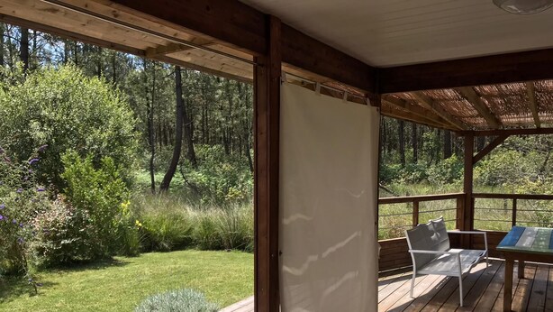 Eine Holzterrasse mit überdachter Sitzgelegenheit, mit Blick auf ein bewaldetes Gebiet.