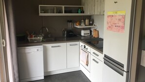 Eine kleine Küche mit weißen Schränken, einem Geschirrspüler von Bosch, einem Kühlschrank und einem Kalender an der Wand.