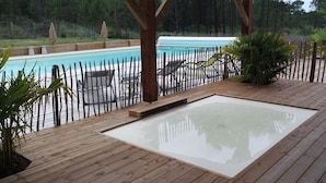 Eine Holzterrasse mit Whirlpool, Liegestühlen und einem Pool.