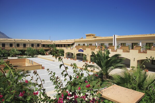 A hotel courtyard with palm trees, a central open space, and a building with a sign reading "Delisaster." - Dolcestate (Campofelice di Roccella)