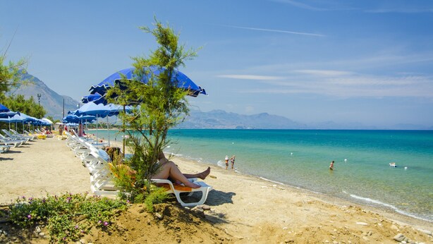Ein Strand mit Liegestühlen, Sonnenschirmen und klarem türkisblauem Wasser.