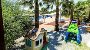Espaço infantil com uma casinha, estrutura de escalada e piscina ao fundo.