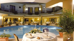 Ein Hotel-Atrium mit einem zentralen Pool, mehreren Essbereichen und einem Balkon mit Geländern.