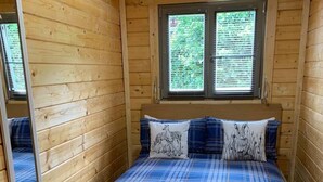 A wooden cabin bedroom with a bed, two pillows with animal prints, a window with blinds, and a mirror on the wall. - Immaculate Cabin 5 Mins to Inverness Dog Friendly (Inverness)