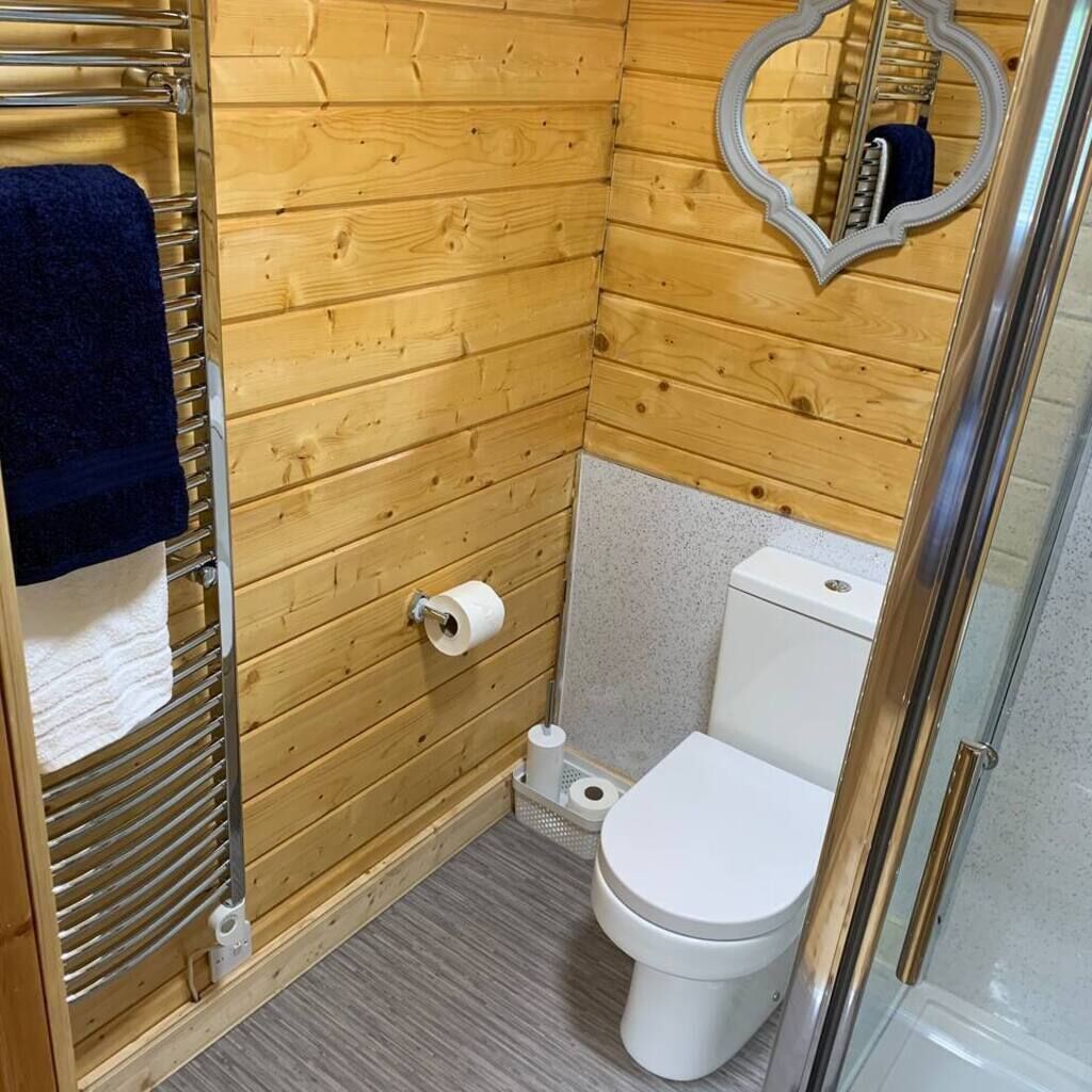 A small, wooden-paneled bathroom with a toilet, a towel rack, and a mirror.