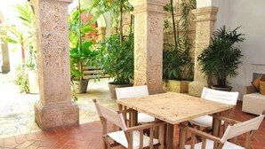 Un patio al aire libre con una mesa y sillas de madera, rodeado de plantas en macetas y pilares de piedra.