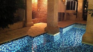 Una piscina interior con suelo de baldosas y paredes de ladrillo, rodeada de columnas y arcos.