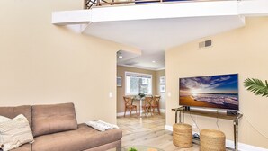 A living room with a brown sofa, a glass coffee table, and a flat-screen TV on a stand. - 1 House from the Sand w/ Rooftop Deck on 28th Street (Newport Beach)